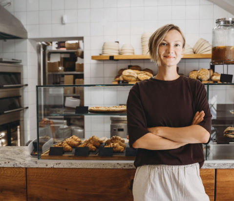 Confident small bakery owner smiling in front of a pastry display case