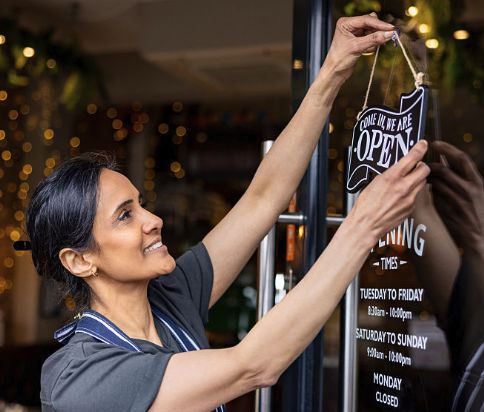 Small business owner hanging a Come In We Are Open sign on the shop door